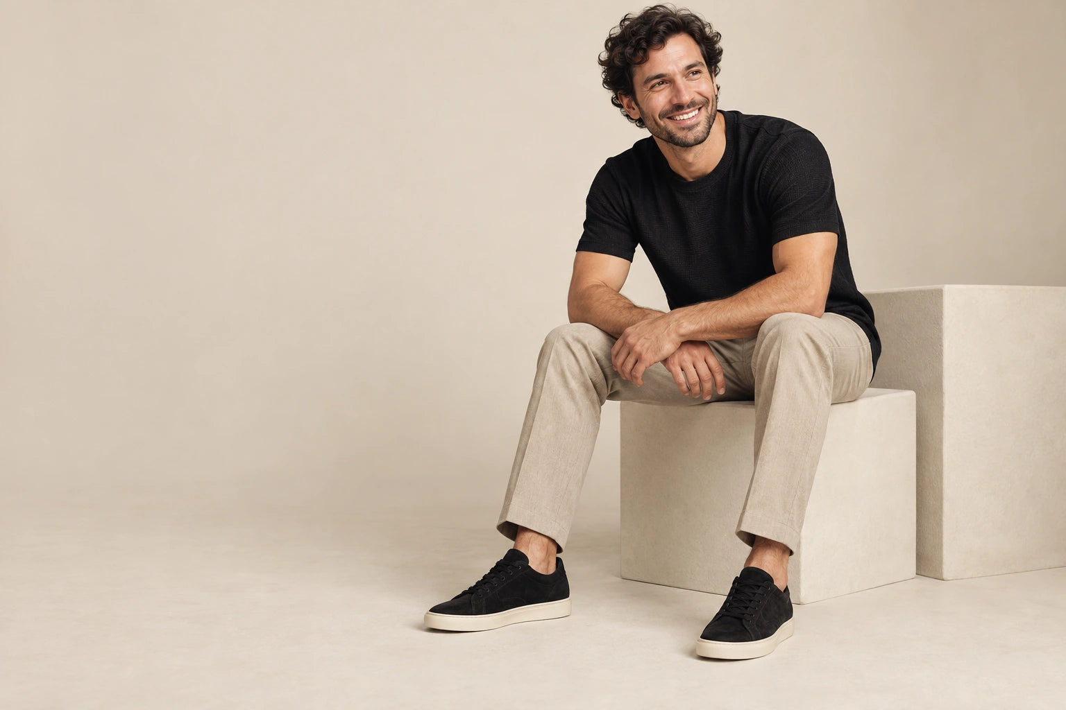 Hombre con tenis negros sentado en un estudio de tonos beige